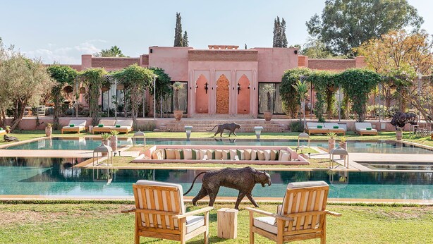 A pool area with lounge chairs, a statue of a leopard, and a building with arched doorways. - Villa Dihya pool and jacuzzi - My Rental Homes (Marrakesh)