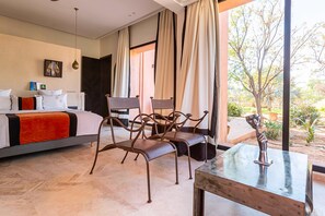 Een slaapkamer met een bed, twee stoelen, een tafel en uitzicht op een tuin.