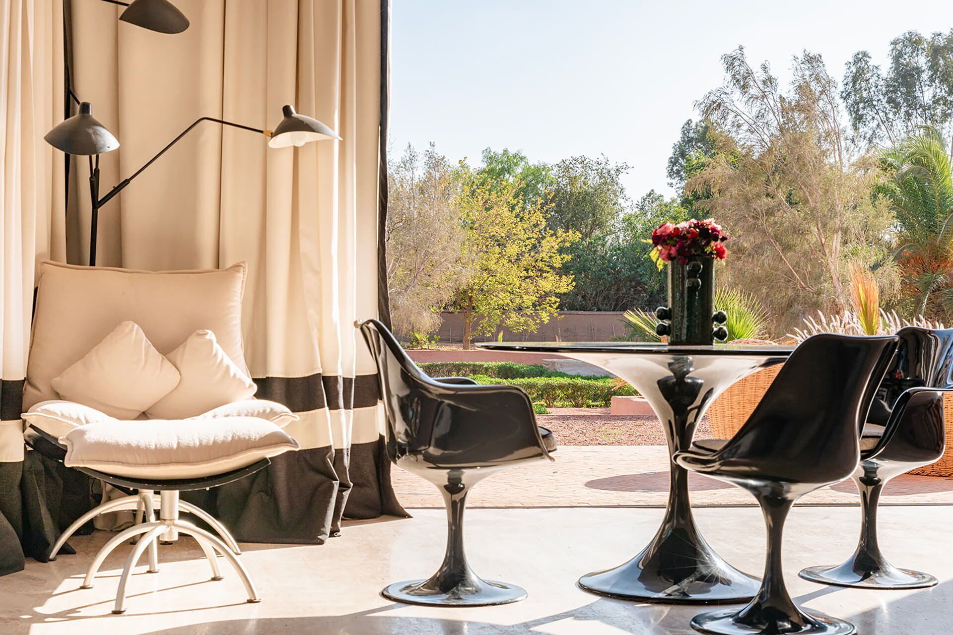 A modern outdoor seating area with a table and chairs, a hanging chair, and a view of a garden.