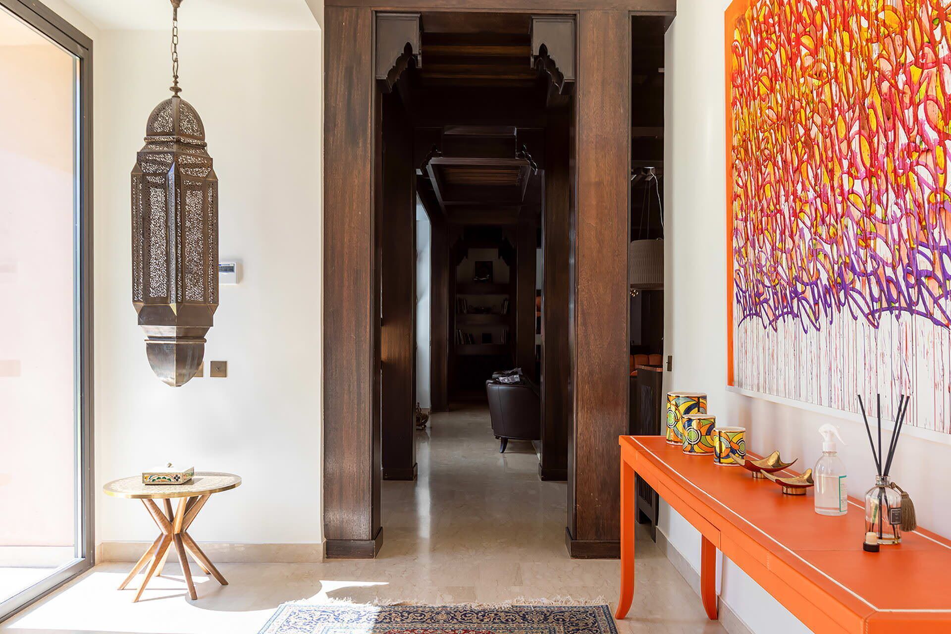 Un couloir orné d’une lanterne traditionnelle, une table ronde avec un coffre, et une peinture abstraite aux couleurs vives accrochée au mur.