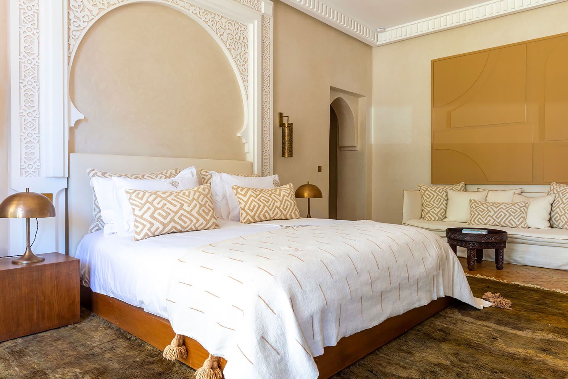A hotel room with a large bed, a sofa, a small table, and a decorative wall.
