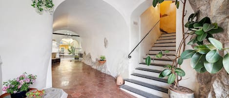 Un pasillo con suelo de baldosas, una escalera y plantas en macetas.