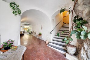 Un couloir avec un sol carrelé, un escalier et des plantes en pot.
