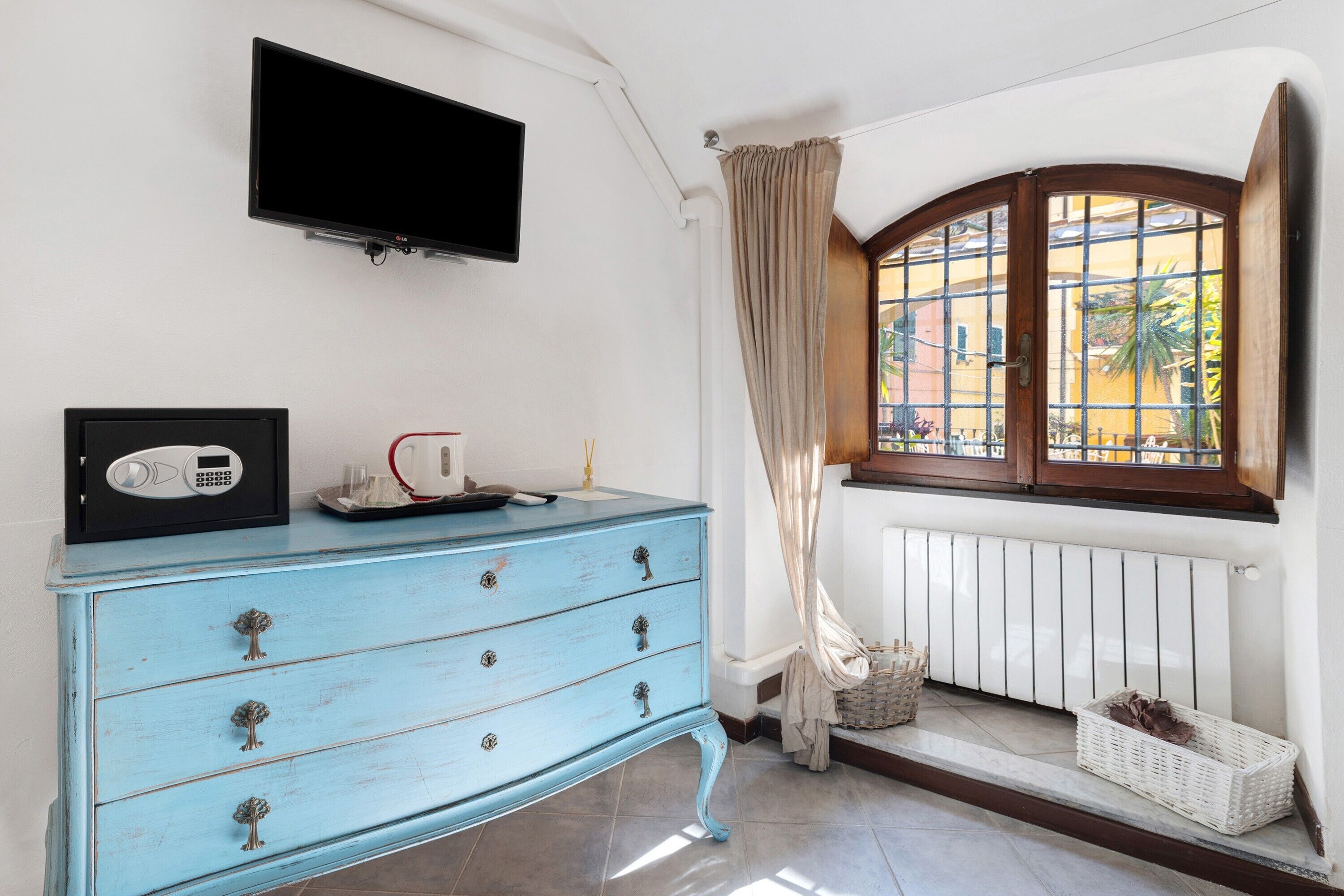 A room with a blue dresser, a television mounted on the wall, a window with a view of buildings, and a radiator.