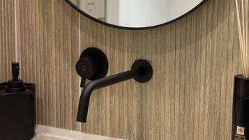 Un baño con un espejo redondo, un grifo negro y un recipiente con palitos de junco.