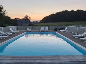 A rectangular swimming pool surrounded by white lounge chairs, with a fence and a house in the background. - Gîte sleeps 20 with swimming pool and large grounds (Languidic)
