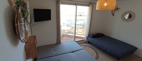 A room with a bed, a TV, a window with curtains, a ceiling light, and a wall decoration.