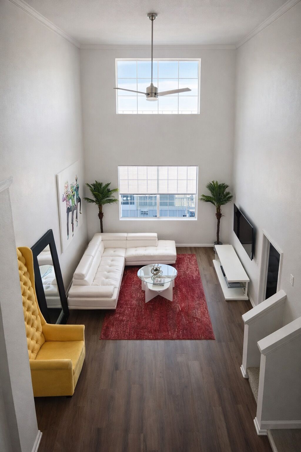 A modern living room with a white sofa, a yellow armchair, a glass coffee table, and two potted plants.