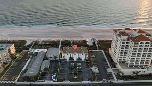 Ilmakuva rannikolla sijaitsevasta hotellista, jossa on parkkipaikka, punaisella merkillä varustettu rakennus ja suuri hotellikompleksi.
