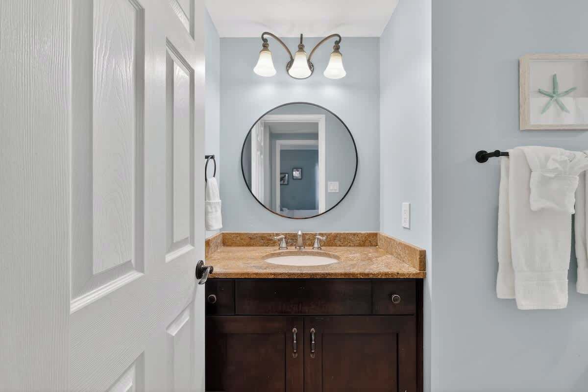 Une salle de bain avec un lavabo, des meubles sombres, un miroir rond et un porte-serviettes.