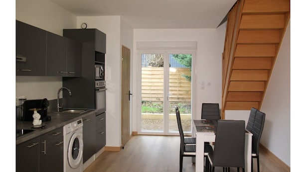 Une cuisine compacte dotée d’appareils électroménagers modernes, un coin repas avec une table et des chaises, et une porte-fenêtre coulissante donnant sur un espace extérieur.