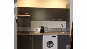 Une cuisine compacte avec des meubles de rangement sombres, un lave-linge encastré, une machine à café et un évier.