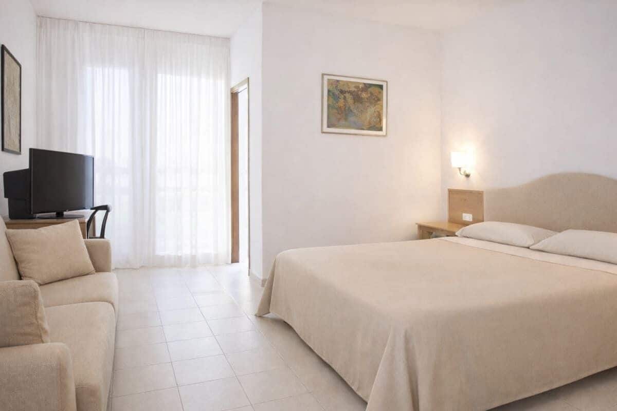 Une chambre d’hôtel avec un lit, un canapé, une télévision, un tableau et une table de chevet avec une lampe.