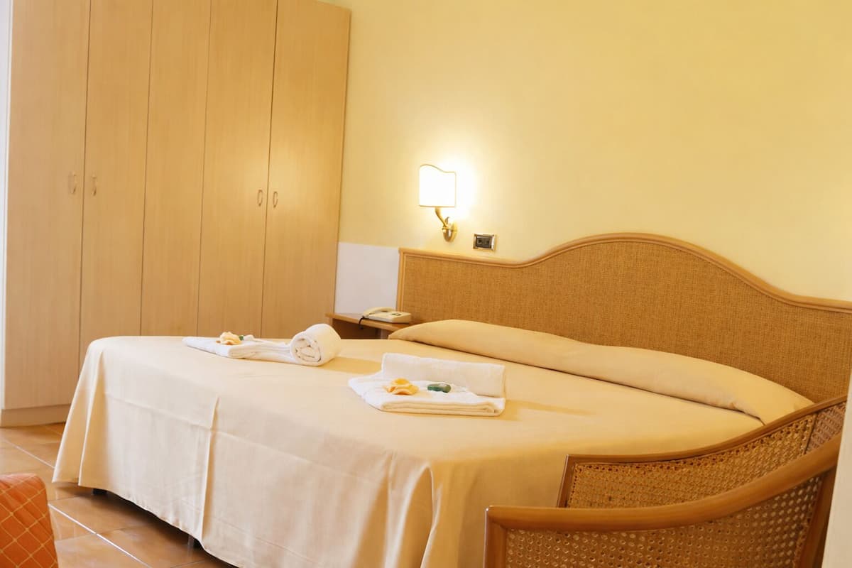 Une chambre d’hôtel avec un lit, une table de chevet, une lampe et une armoire.