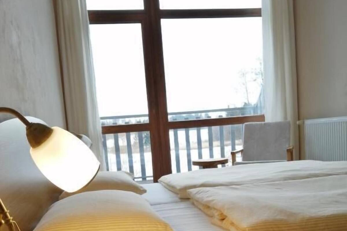 Une chambre d’hôtel avec un lit, une table de chevet, une lampe, une chaise et une vue sur l’extérieur.