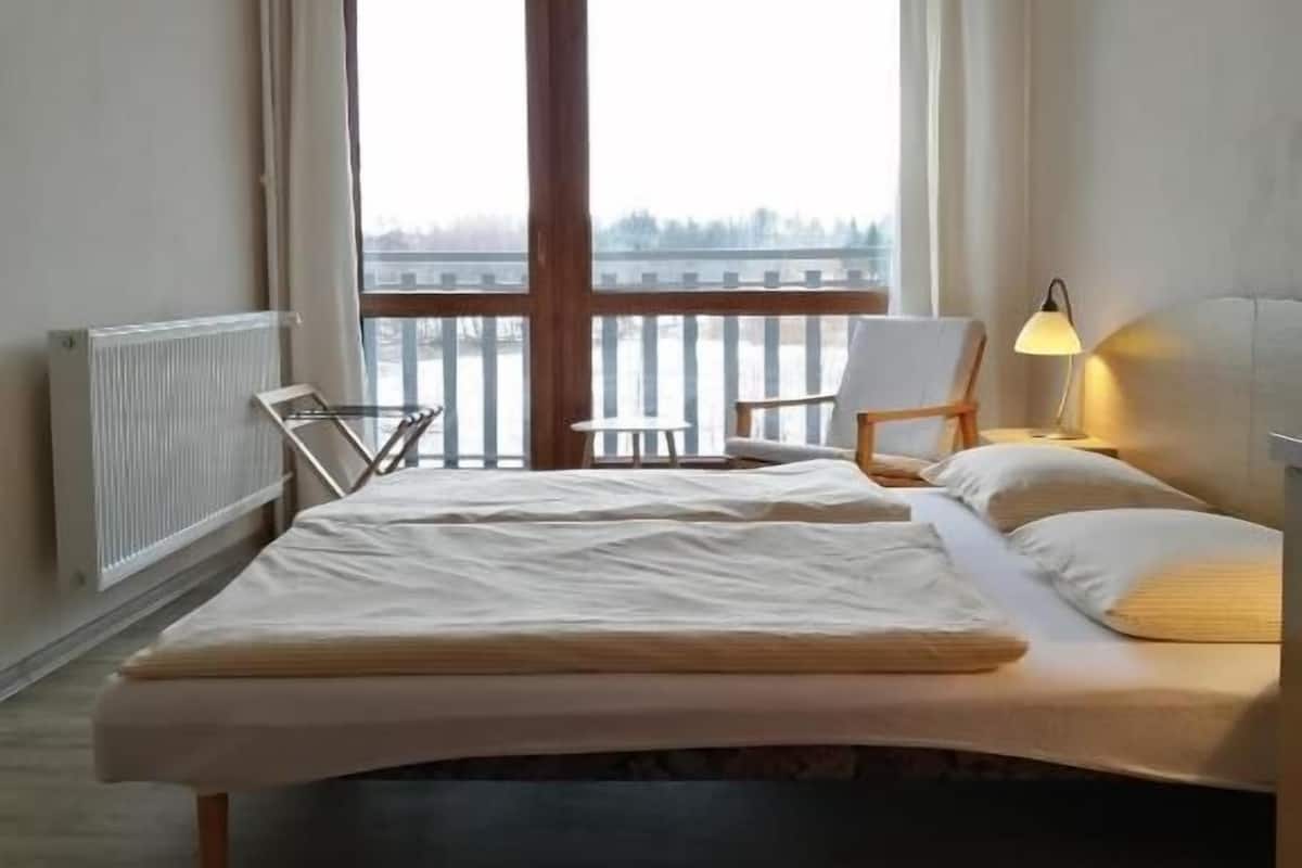 Une chambre à coucher avec un lit, une chaise, une lampe et une vue sur l’extérieur grâce à une grande fenêtre.