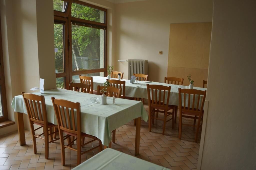 Un espace repas comprenant plusieurs tables et chaises, de grandes fenêtres et un radiateur.