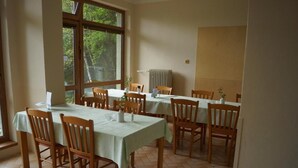 A dining area with multiple tables and chairs, large windows, and a radiator. - Hotel Chytrov (Volfířov)