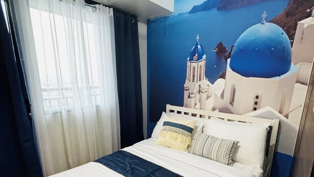 Ein Hotelzimmer mit Bett, Vorhängen, einer Klimaanlage und einem Wandbild eines Gebäudes mit blauer Kuppel.