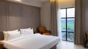 A modern hotel room with a large bed, a nightstand, a chair, a ceiling fan, and a large window with a view.