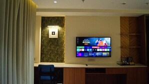 A hotel room with a flat-screen TV mounted on the wall, a wooden entertainment unit, a blue chair, and a curtain.