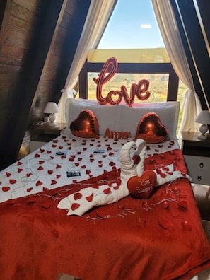 A bedroom with a bed, a window with curtains, a decorative sign, and a bedside table with a lamp.