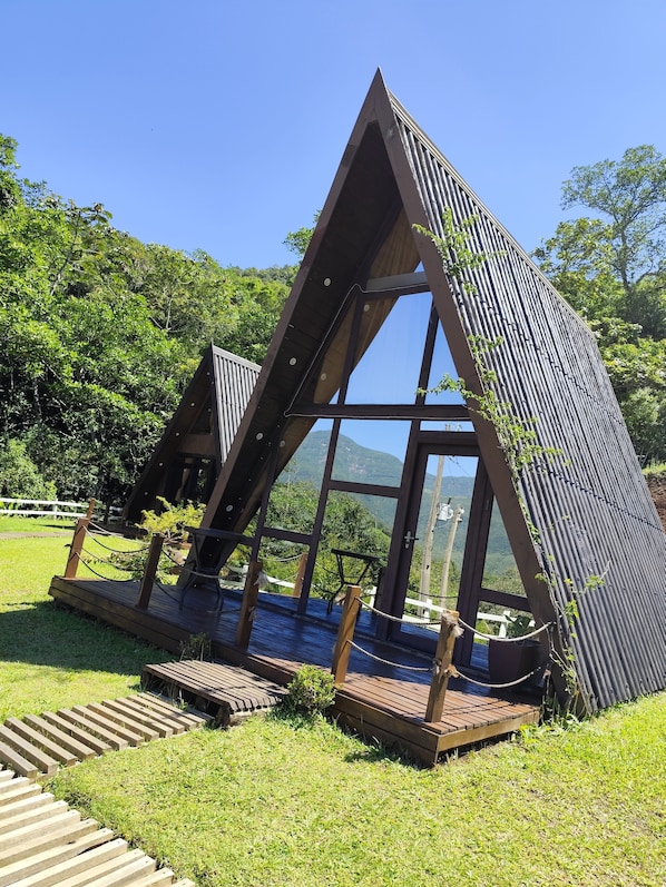 A triangular wooden structure with a glass viewing area, surrounded by a grassy area and trees.