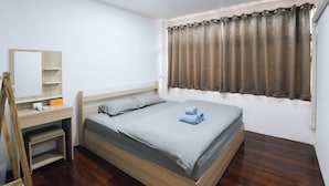 A bedroom with a bed, a desk, a mirror, and a window with curtains.