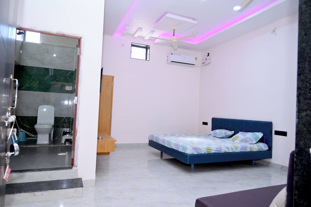 A bedroom with a bed, a ceiling fan, an air conditioning unit, and a small window.
