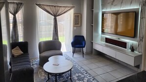 Ein modernes Wohnzimmer mit Sofa, Sessel, Couchtisch und einem an der Wand befestigten Fernseher.
