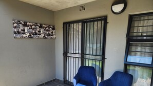 Ein Zimmer mit Fliesenboden, einem an der Wand hängenden Bild von Tieren, einer Gittertür und zwei blauen Stühlen.