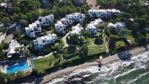 An aerial view of a coastal residential area with white buildings, a swimming pool, and a beach. - Captain Jack’s Seaside Villa (Nea Makri)