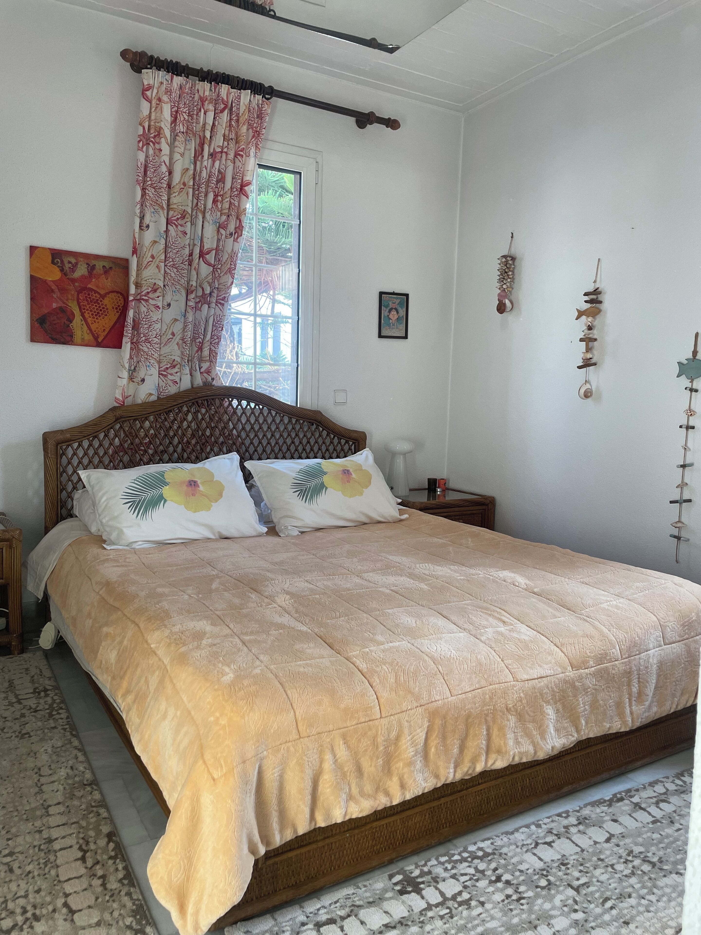 Uma cama com colcha florida, cabeceira de madeira e janela com cortina.