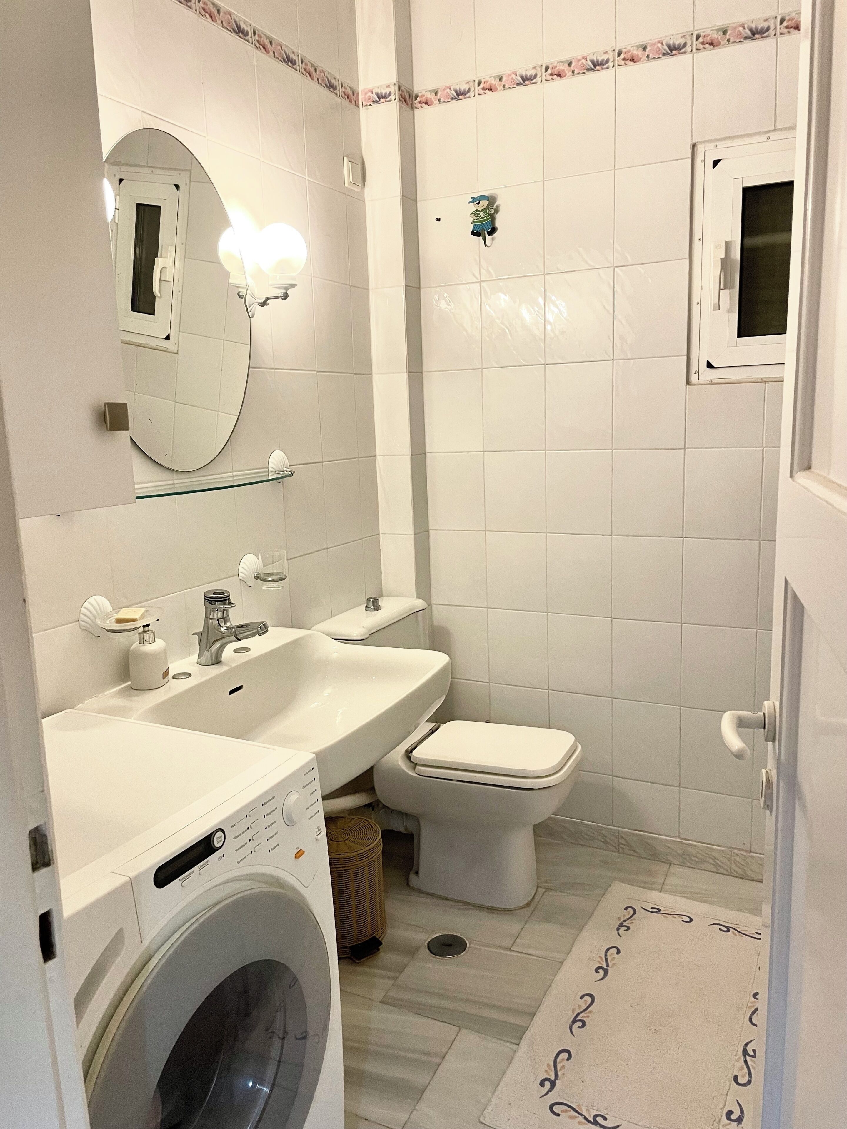 A bathroom with a washing machine, sink, toilet, and a mirror.
