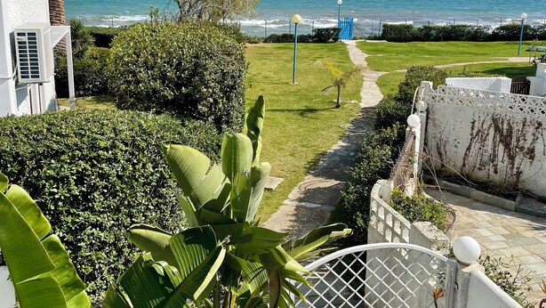 A coastal view with a pathway leading to the sea, surrounded by lush greenery and a white building. - Captain Jack’s Seaside Villa (Nea Makri)