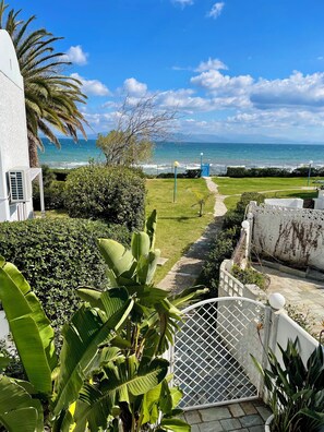 A coastal view with a pathway leading to the sea, surrounded by lush greenery and a white building. - Captain Jack’s Seaside Villa (Nea Makri)