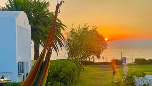 A hammock on a balcony overlooking a sunset, a body of water, and a grassy area with a pathway. - Captain Jack’s Seaside Villa (Nea Makri)