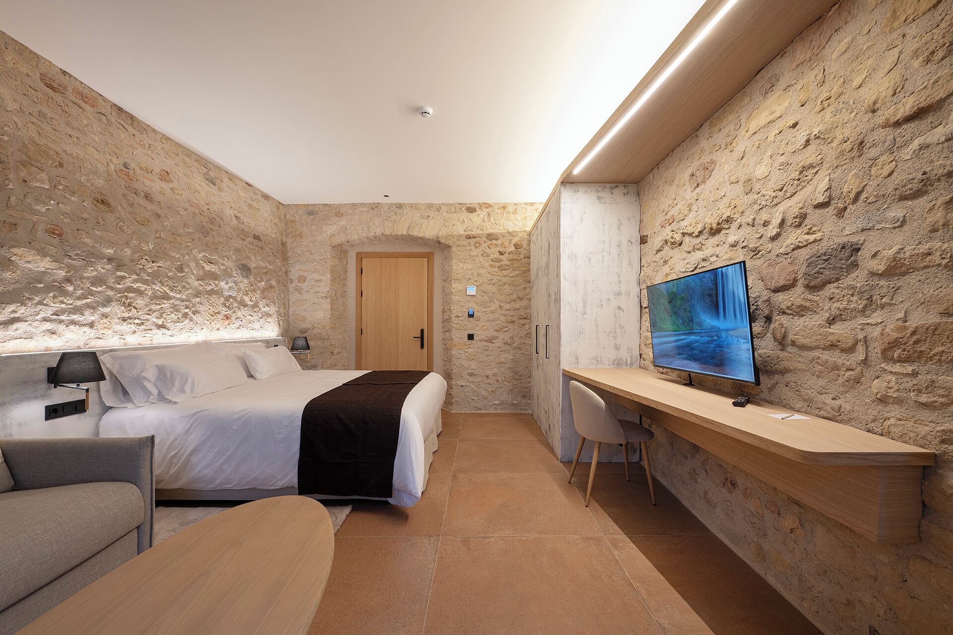 Ein gemütliches Hotelzimmer mit Steinwand, einem Bett, einem Schreibtisch und einem Fernseher.