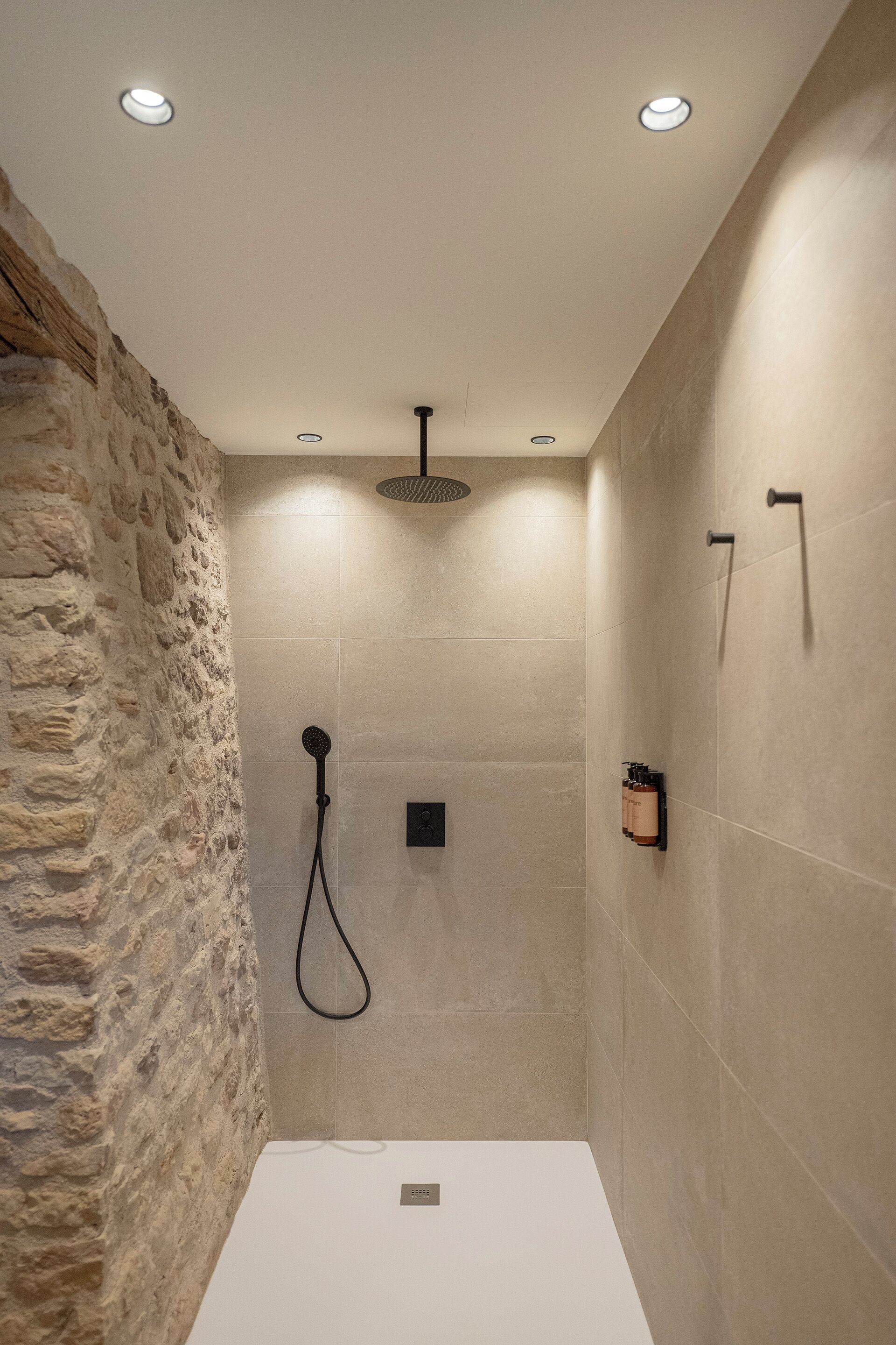 A modern shower with a stone wall, recessed lighting, and a minimalist design.