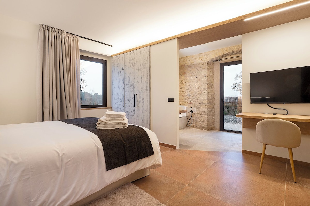 A bedroom with a bed, a desk, a chair, a TV, and a bathroom with a shower.