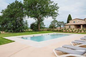 Una piscina con lettini, circondata da un prato curato e alberi.