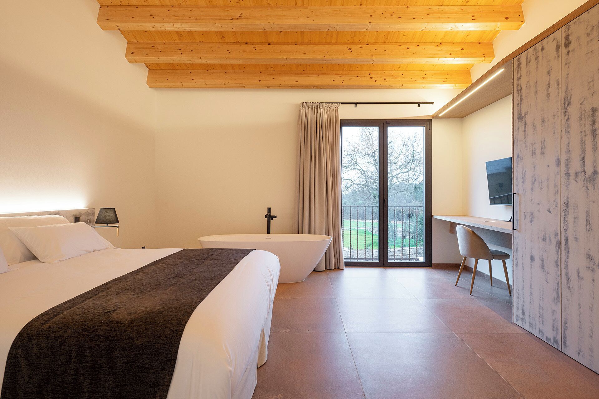 Una habitación de hotel moderna con techo de madera, una cama, un escritorio, una silla y un ventanal con vistas.