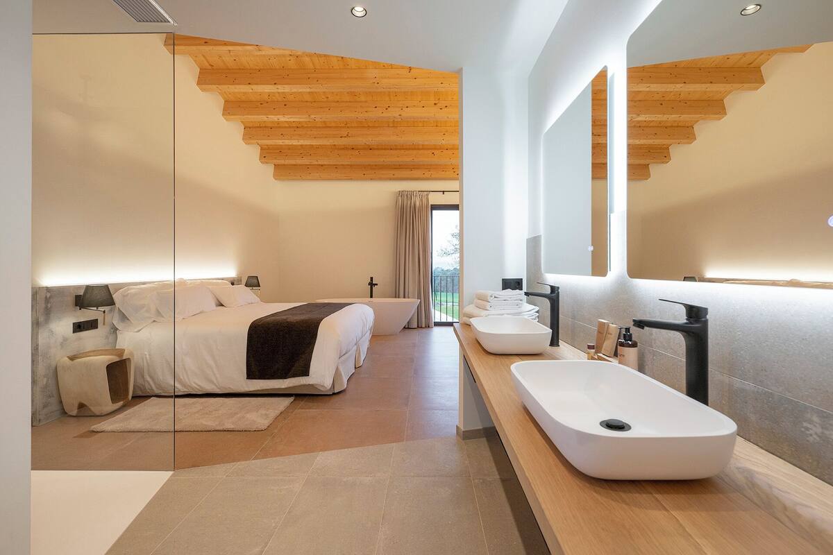 A modern bedroom with a large bed, bedside tables, a bedside lamp, and a view through a window.