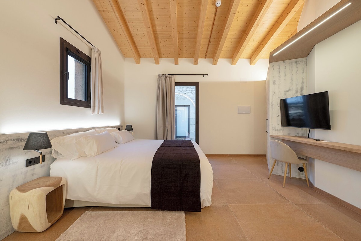 A bedroom with a bed, bedside table, lamp, and a TV.