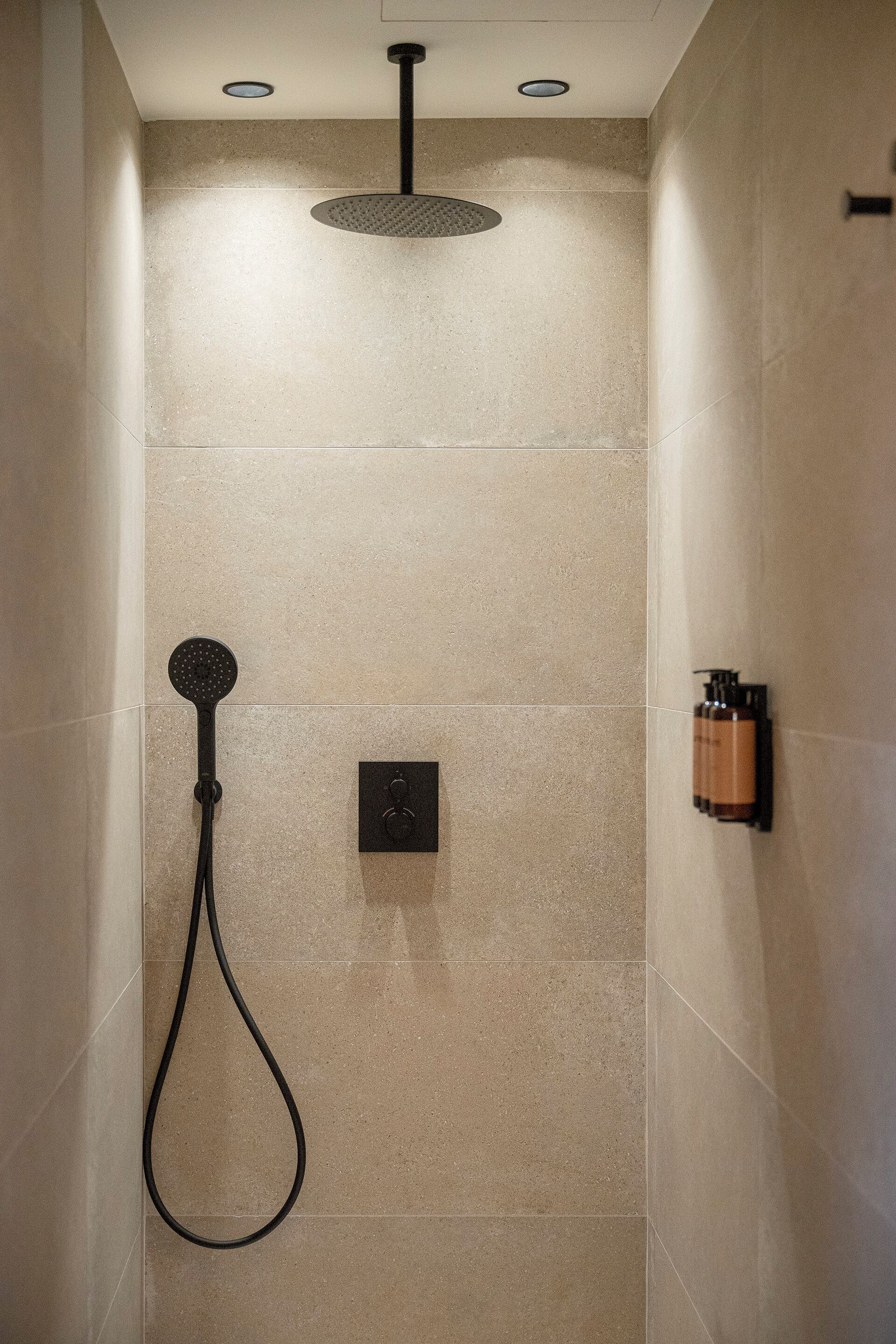 A shower with a handheld showerhead, a wall-mounted control panel, and a bottle of shampoo.