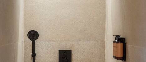 A shower with a handheld showerhead, a wall-mounted control panel, and a bottle of shampoo.