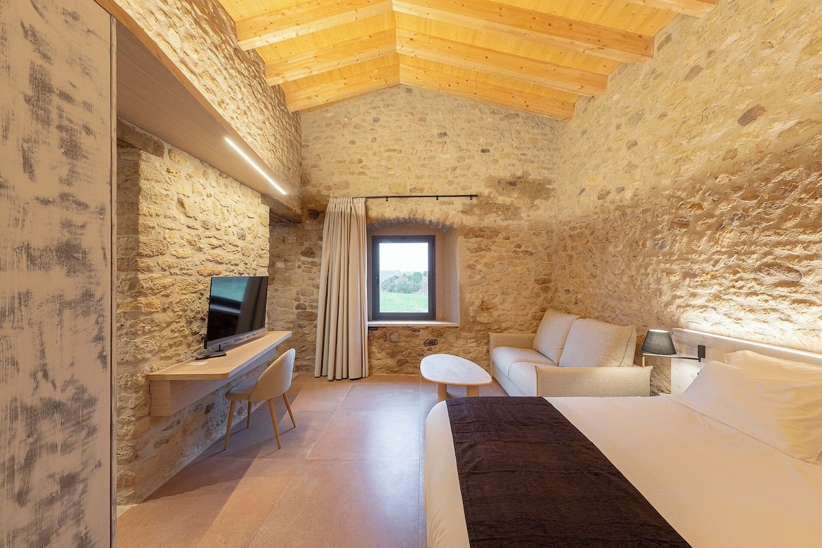 A cozy room with a stone wall, wooden ceiling, a TV, a small table, a sofa, and a window.