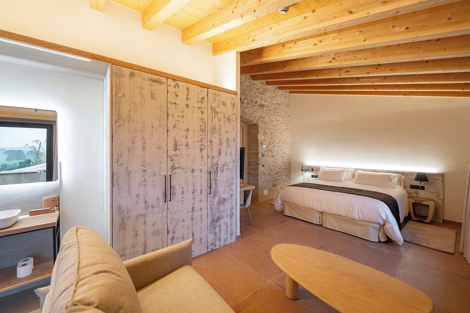 A bedroom with a bed, bedside table, and a stone wall.