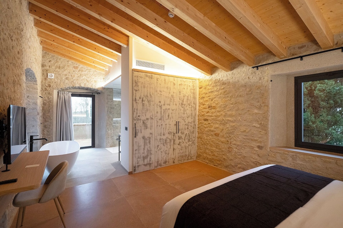 A bedroom with a bed, a desk, and a chair. There is a window and a door leading to another room.