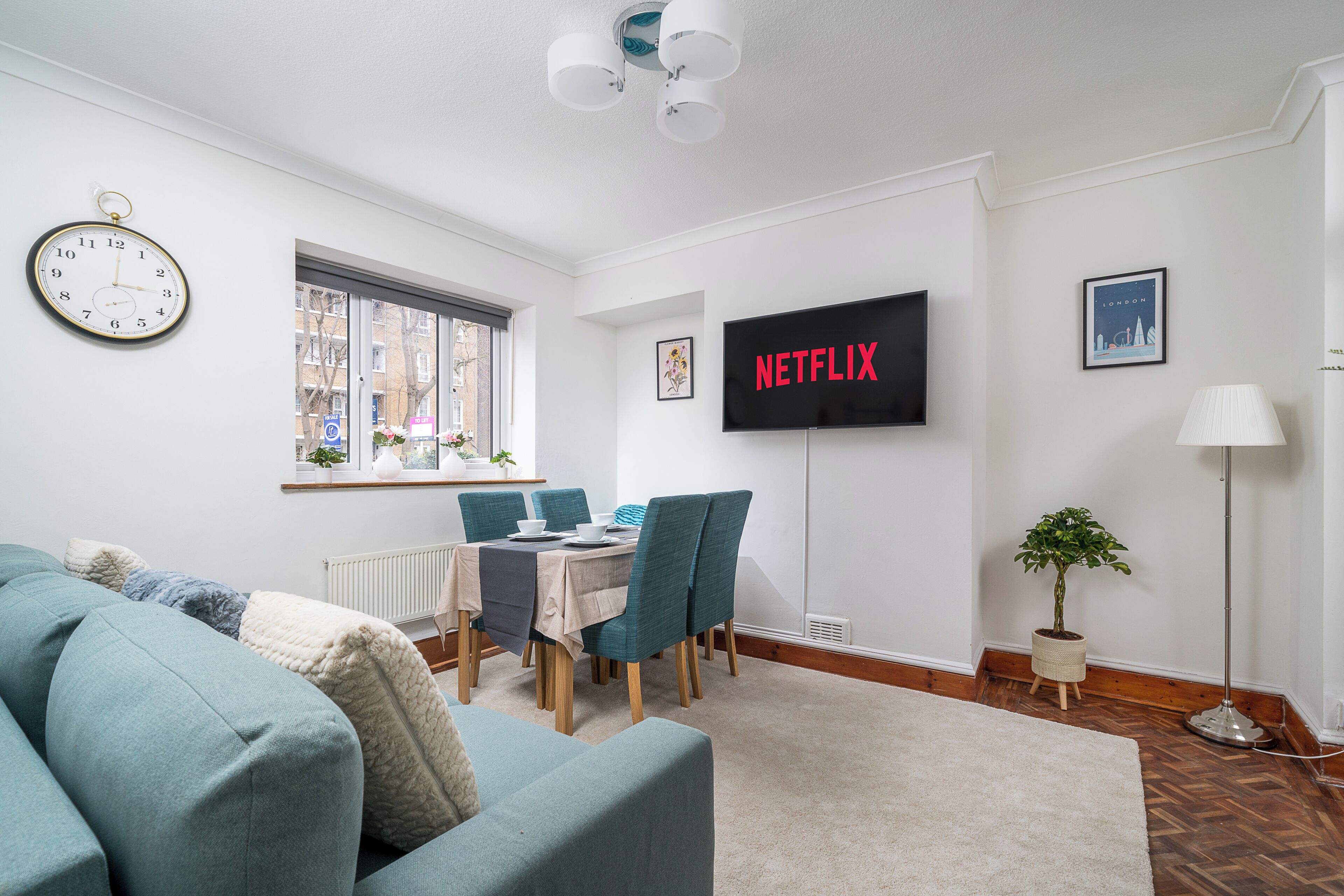 Ett modernt vardagsrum med en soffa, ett matbord, stolar, en tv, en klocka och en krukväxt.